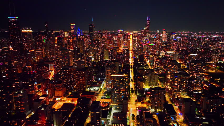 Illuminated Chicago skyline at night along Michigan Avenue, Illinois. Elevated perspective shows a bright avenue cutting through dense towers toward the horizon.