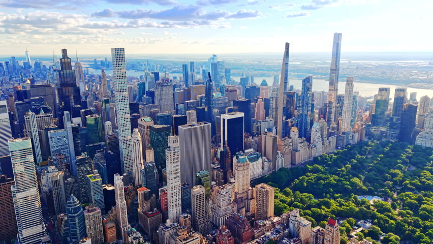 Aerial view of Manhattan skyline toward Central park south, New York City. Hudson river visible beyond towers under bright blue sky.