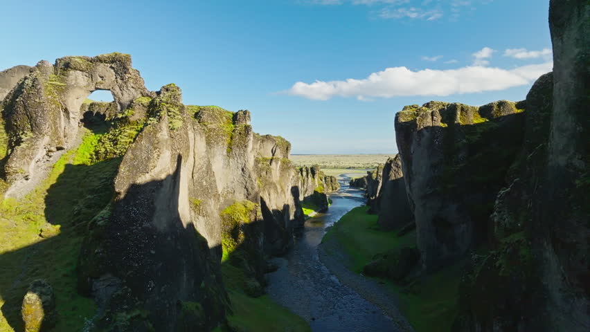 Cinematic forward drone flight through the spectacular Fjaðrárgljúfur Canyon in Iceland revealing towering basalt cliffs lush moss-covered walls and a winding glacial river below.