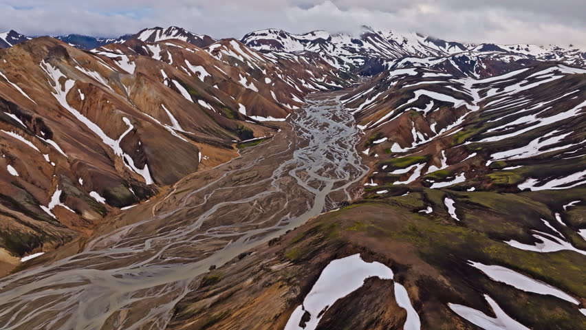 Cinematic forward drone flight through Iceland’s Rainbow Mountains following braided glacial rivers between colorful rhyolite peaks revealing the remote beauty of the volcanic Highlands.