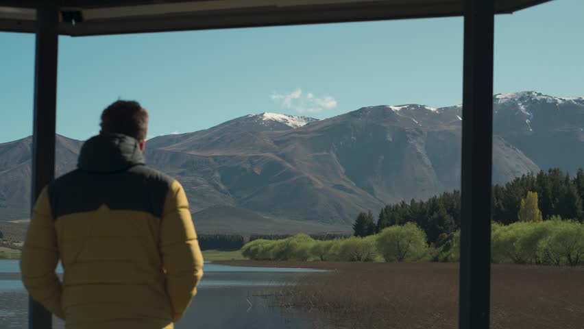 Man in a yellow jacket standing on a wooden pier looking towards the mountains at Laguna La Zeta, Esquel, Chubut, Argentina.