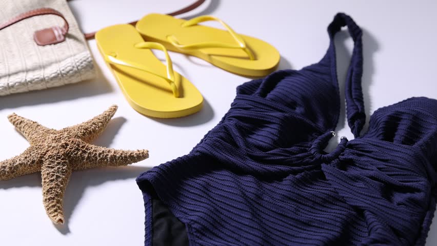 Woman putting stylish sunglasses onto swimsuit on light grey background, closeup