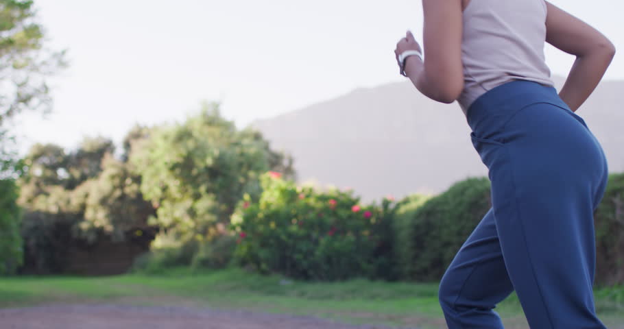 African American woman jogging as camera tracks on gravel path showing fitness watch for exercise. Runner, outdoor, trail, nature, running, sunlight, daylight
