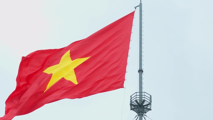 The Vietnamese national flag waves at close range on a tall pole against an overcast sky in Hue, Vietnam.