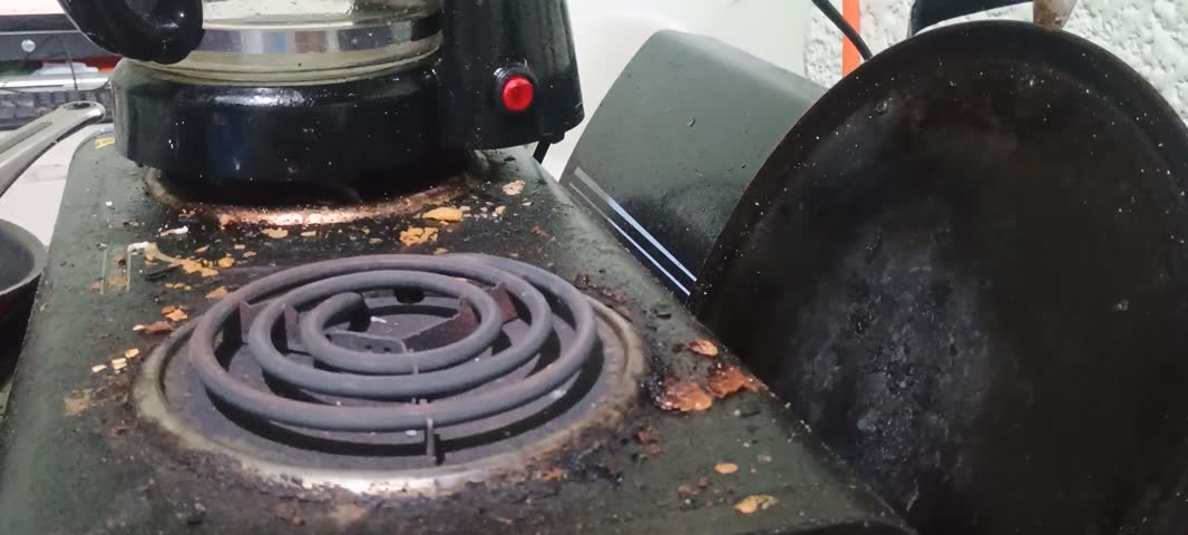 Side view of a person placing a small pot on an electric stove burner and pouring cooked whole beans with broth into it.