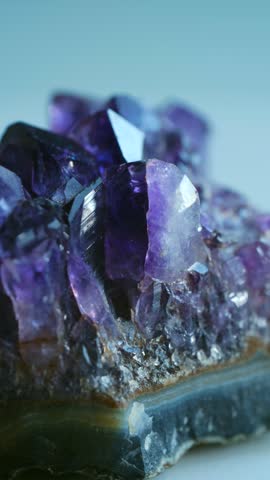 Beautiful purple amethyst crystal cluster with sparkling facets slowly rotating on white background, showing its raw, natural mineral structure. Vertical. Purple amethyst crystal geode slowly rotating