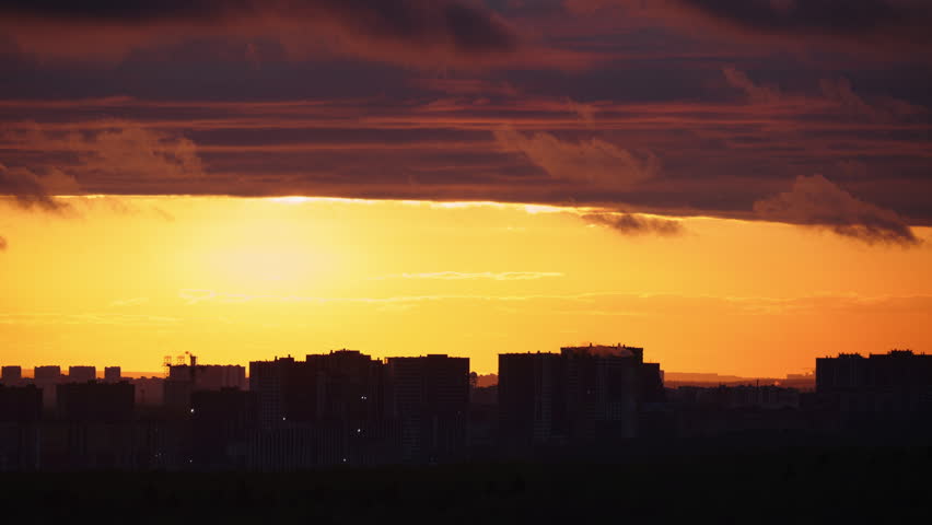 Orange sunset over a city skyline. Silhouette of urban buildings under a golden evening sky. Scenic view of metropolitan cityscape and horizon during dramatic twilight glow.