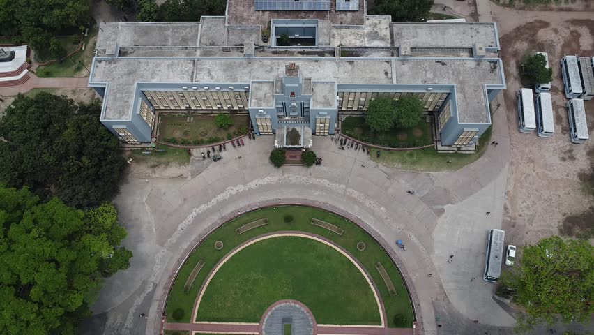 Aerial view of a large university administrative building with a circular garden courtyard and parked buses on a clear day administration drone campus education architecture