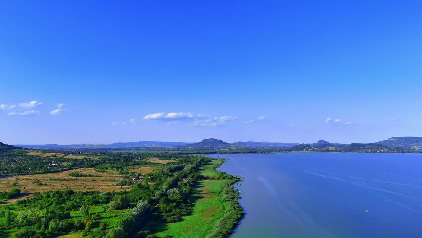 Daytime lake and greenery. A large lake surrounded by green fields and hills under a clear blue sky.