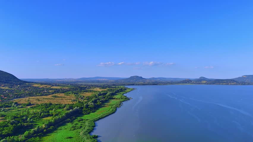 Lake with hills behind it. A large lake stretches out with green land on the shore and hills visible in the distance during a clear day.