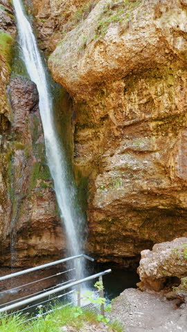 Narrow waterfall falling from the sandstones. Low angle view at the cataract among the bare rocks. Vertical video.