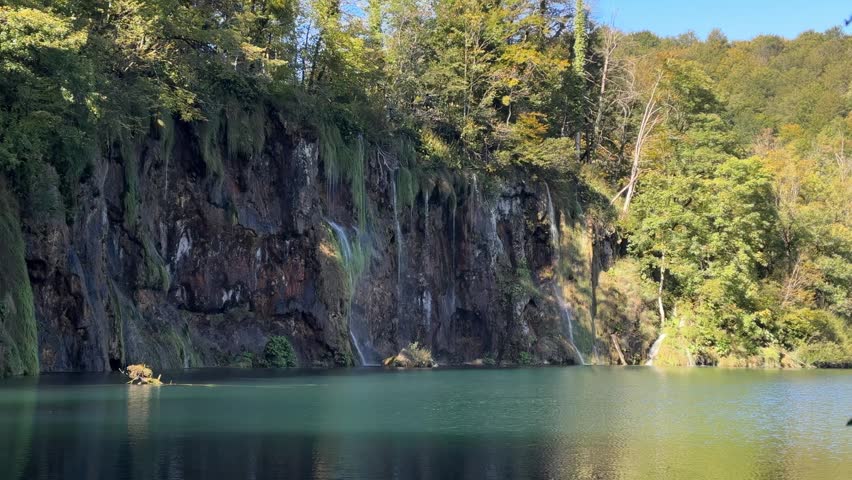 Plitvice Lakes National Park, Croatia. Scenic waterfall cascading into tranquil lake surrounded by lush greenery and vibrant autumn foliage in nature