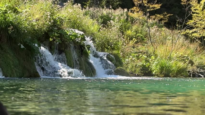 Plitvice Lakes National Park, Croatia. Scenic waterfall cascading into tranquil lake surrounded by lush greenery and vibrant autumn foliage in nature