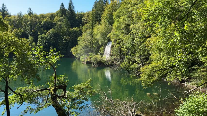 Plitvice Lakes National Park, Croatia. Majestic waterfall cascading down rocky cliff surrounded by lush greenery and blue sky in natural landscape
