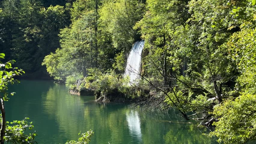 Plitvice Lakes National Park, Croatia. Majestic waterfall cascading down rocky cliff surrounded by lush greenery and blue sky in natural landscape
