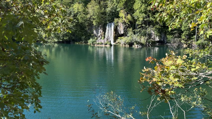 Plitvice Lakes National Park, Croatia. Majestic waterfall cascading down rocky cliff surrounded by lush greenery and blue sky in natural landscape
