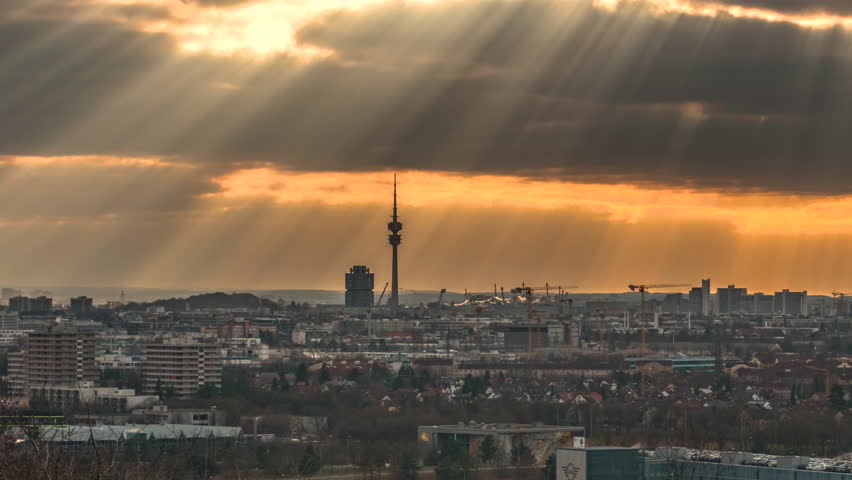 Timelapse of the Munich skyline featuring dramatic sun rays breaking through storm clouds above the city under a spectacular evening sky in Bavaria, Germany.