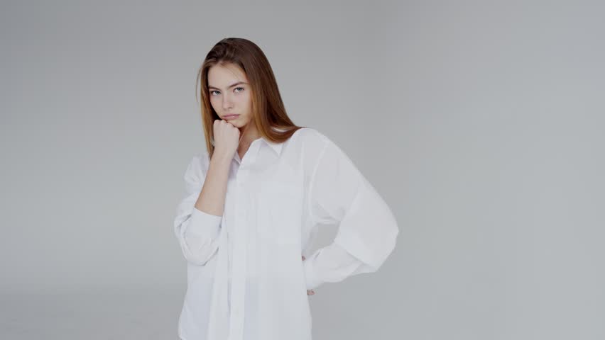 A portrait of a young Caucasian woman wearing a white shirt, posing confidently in front of a grey background. Her light brown hair and blue eyes suggest a calm yet assertive demeanor.