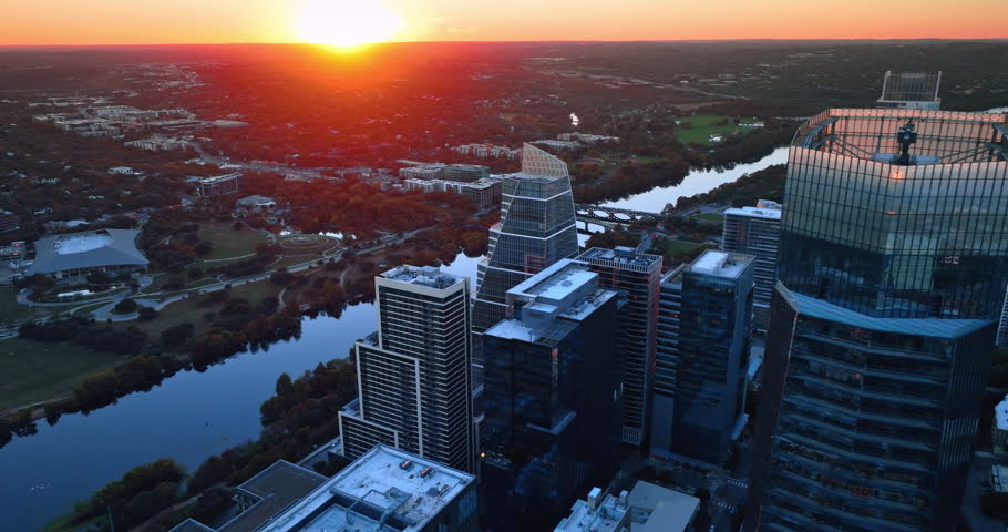 Splendid setting sun over the vast city panorama. Drone footage approaching the top of the high-rise at the waterfront of the Colorado River. Austin, Texas, USA.
