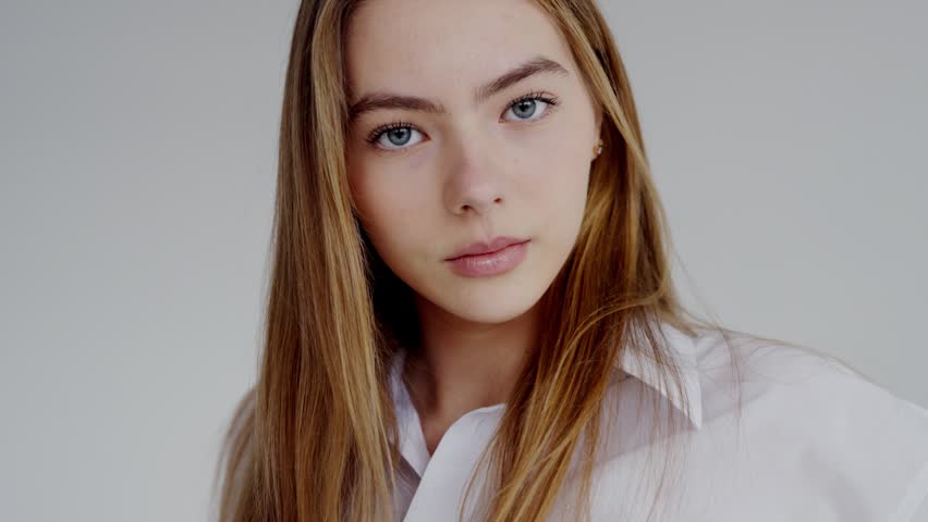 Close-up portrait of a serene young woman with long blonde hair and clear blue eyes, wearing a crisp white shirt. Serene Young Woman in White Shirt Gazing with Confident Eyes