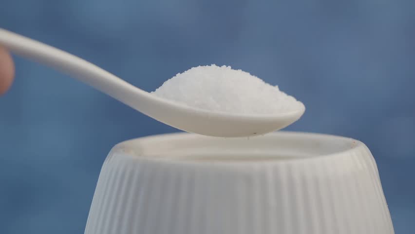Spoon filled with salt held above a white container for cooking.