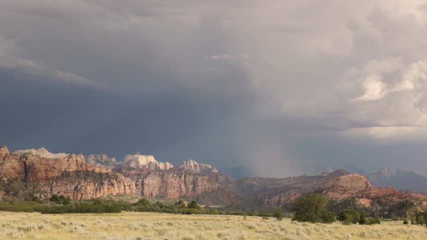 Lightning strikes the mountains of Zion National Park, Utah USA during a summer thunderstorm while sunshine breaks through the clouds and lights the rugged cliffs of West Temple Mountain, seen from the edge of an open field on the Kolob Terrace Road.