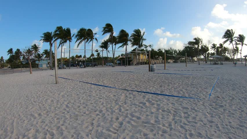Vertical POV walk toward beach volleyball courts at Sombrero Beach in Florida at sunrise with golden light, palm trees and a tropical coastal atmosphere.