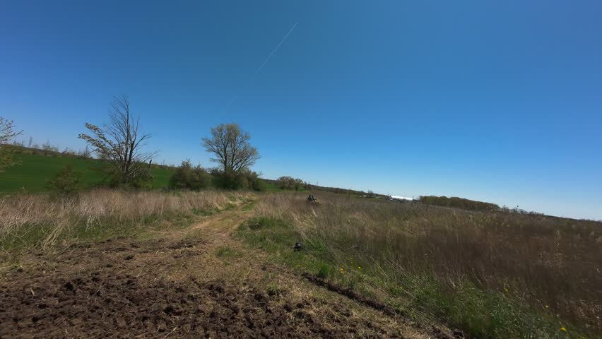 Low angle aerial shot flying over an all-terrain vehicle driving on a narrow trail across an open countryside field on a clear sunny day.