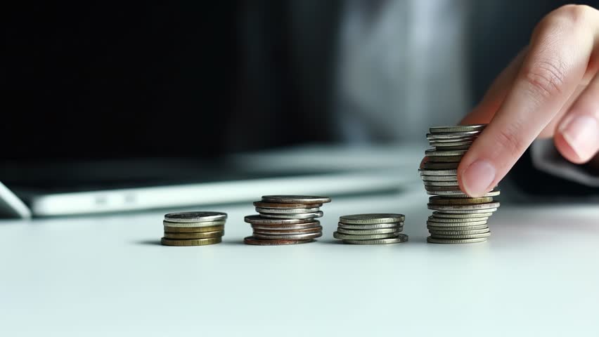 A hand reaches for a stack of coins on a table. The background shows a computer. The scene highlights the importance of SEO in business growth.