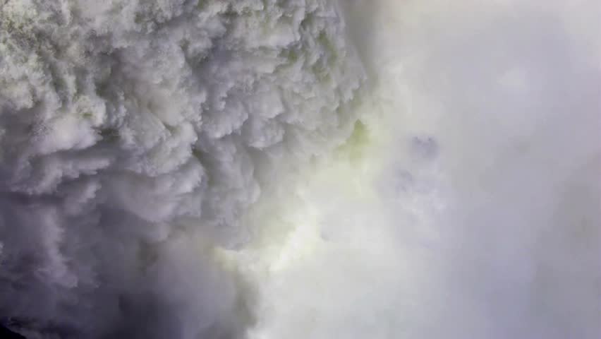 Extreme close up shot of powerful rushing water spraying whitewater foam and mist over a dramatic steep waterfall drop