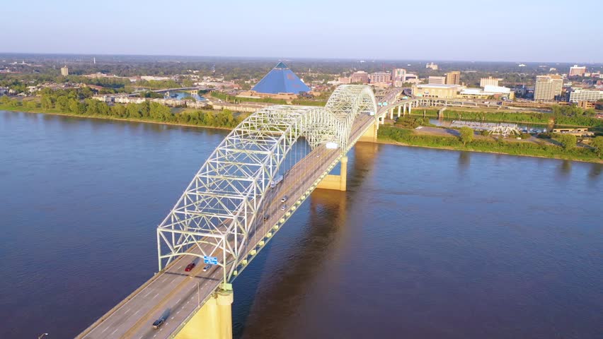 Aerial view of Hernando de Soto steel bridge over Mississippi river in Memphis Tennessee at sunset with moving traffic, cinematic cityscape footage showing urban infrastructure.
