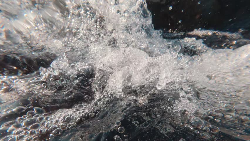 Split level, camera slowly descends underwater into stormy stream of mountain stream. Endless flow of air bubbles under surface of water, Close-up video, Slow motion, Half water shot