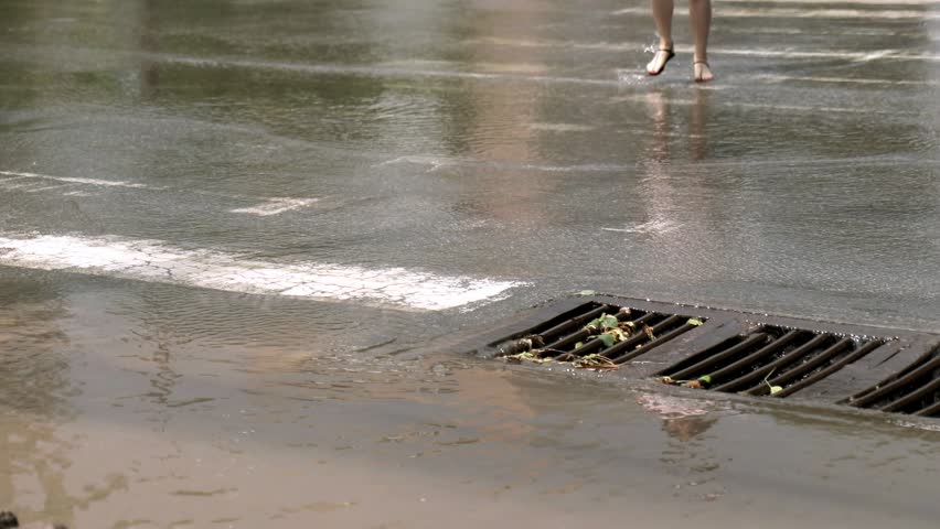 Low angle view of female legs in sandals stepping through a deep puddle on a flooded crosswalk in the city after a heavy downpour