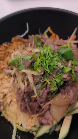 Close up of a person mixing and eating a traditional vietnamese bun bo nam bo noodle salad, a tasty dish with beef, herbs, and peanuts