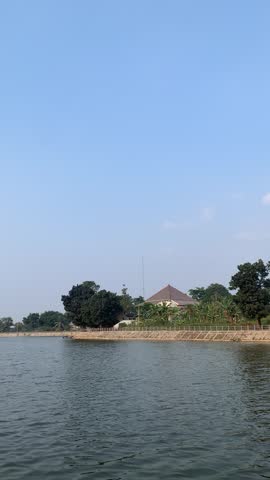 Peaceful rural landscape featuring a calm lake and a traditional house under a clear blue sky