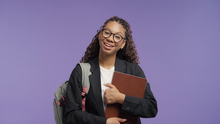 Confident teenage student girl wearing glasses, holding folder, laptop, backpack with natural smile. College woman or young professional prepared for education, business opportunities