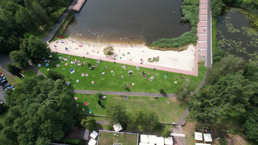 Top-down aerial shot of people relaxing, sunbathing, and swimming at a lake beach on a summer day