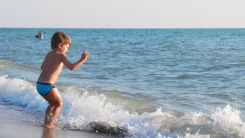 Young Boy Playing and Splashing in Ocean Waves on a Sandy Beach