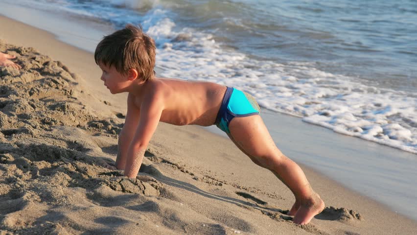 Young Boy Playing and Splashing on the Sunny Sandy Beach Shoreline