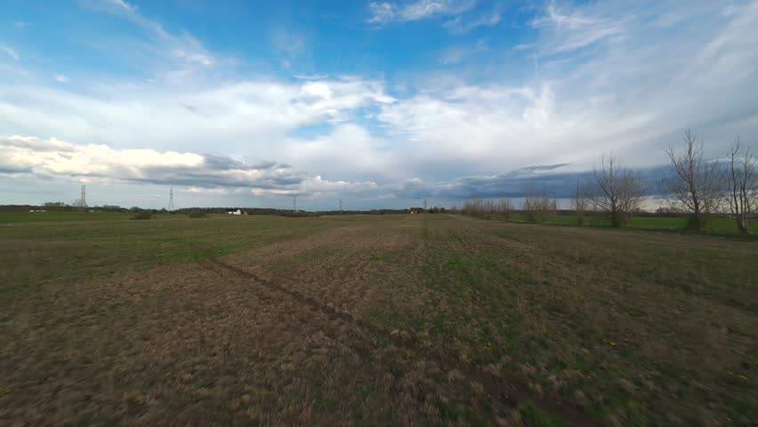 Wide aerial shot tracking forward across an empty rural field of dry grass towards the horizon under a dramatic blue sky with white clouds in Ontario.