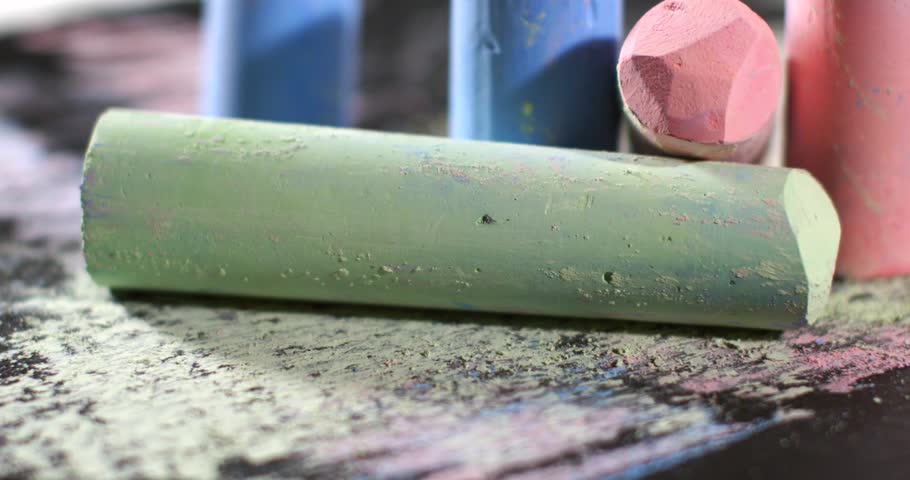 Chalk sticks in multiple colors are scattered on a black surface. Some chalk pieces are broken, showing vivid colors like green, blue, pink, and orange.