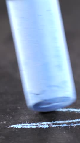 A piece of blue chalk creates a line on a dark surface. The movement of the chalk is captured closely, showing texture and color contrast.
