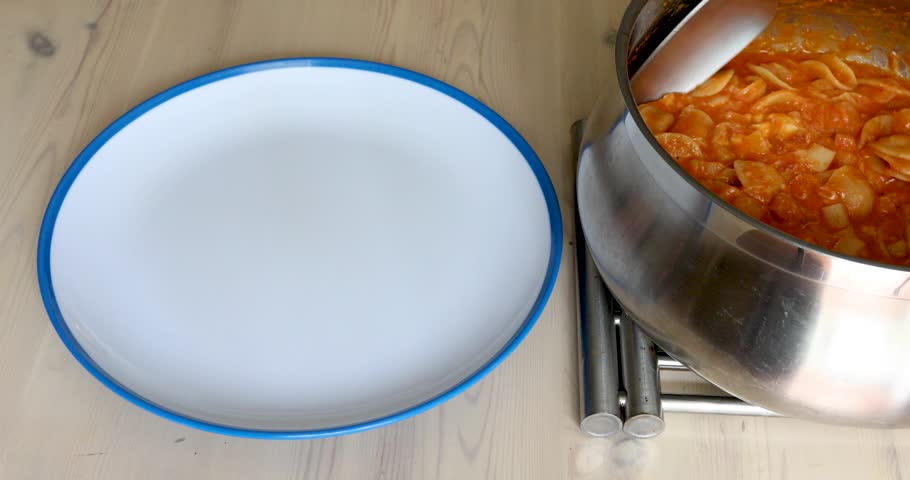 Large spoonfuls of hot short pasta with tomato sauce and melted, stringy cheese served from a stainless steel pot onto a plate. Traditional Italian comfort food.