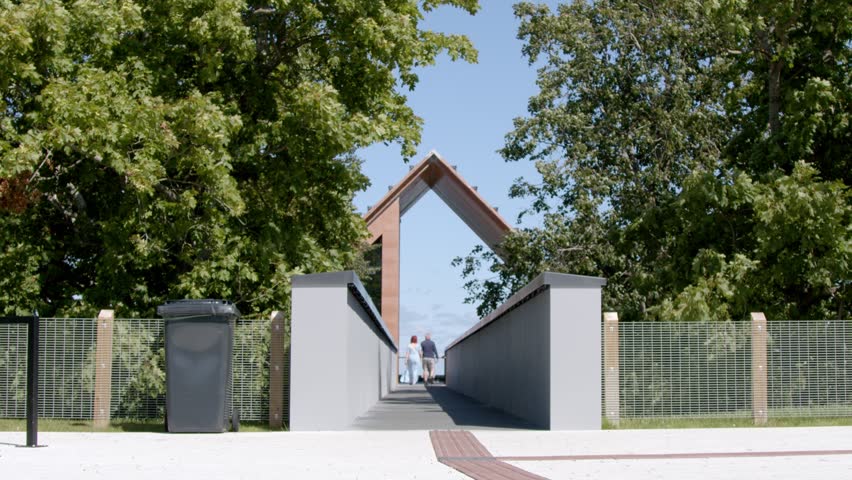 Visitors walking across the modern observation bridge on Muraste Nature Trail before stopping to look down at the landscape below. Peaceful outdoor recreation surrounded by lush summer trees near Tallinn, Estonia.