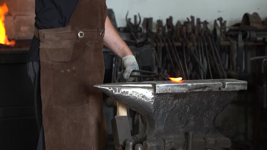 Craftsman in Action: A Skilled Blacksmith Forging Metal with Precision at the Anvil, Highlighting the Art of Traditional Metalworking in a Workshop Setting