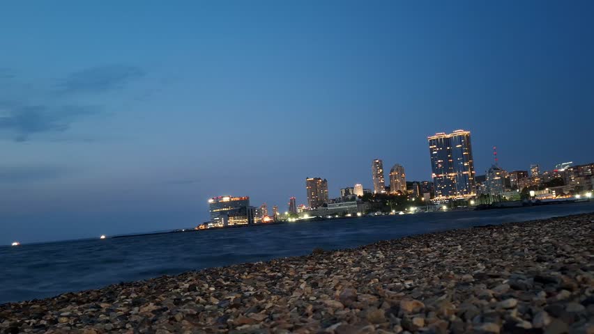 Coastal city lights glowing at dusk beside the sea. Waterfront skyline, evening travel, urban landscape, vacation destination.
