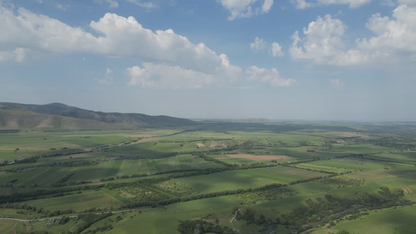 Aerial view of green agricultural fields and hills under a cloudy sky.