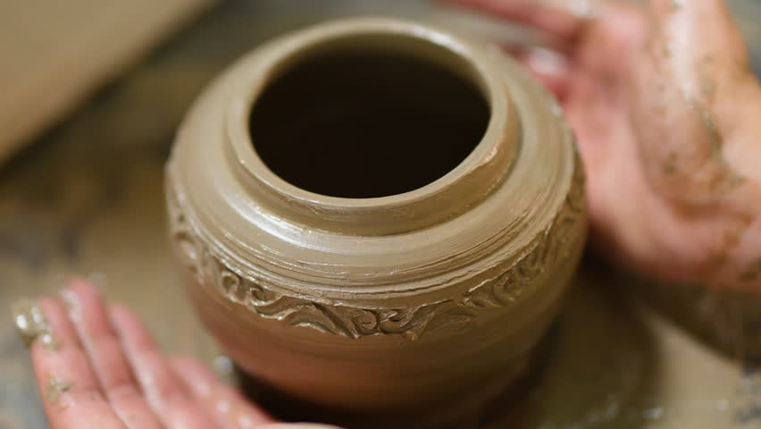 Close-up of hands molding a decorative clay pot on a potter