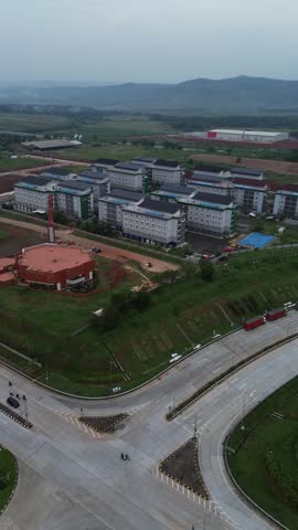 Aerial view of a modern residential apartment complex located near a major highway road with green surrounding hills in the background.