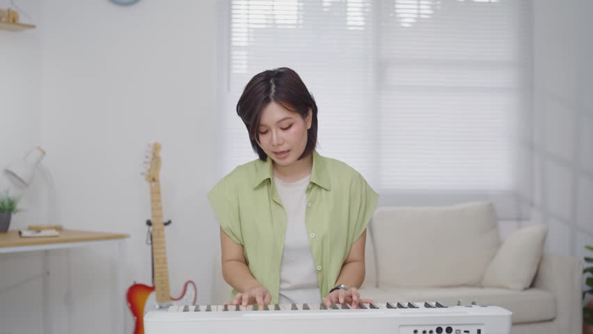 Asian Woman Playing Electronic Keyboard Piano and singing in Living Room at Home for Music Practice Concept